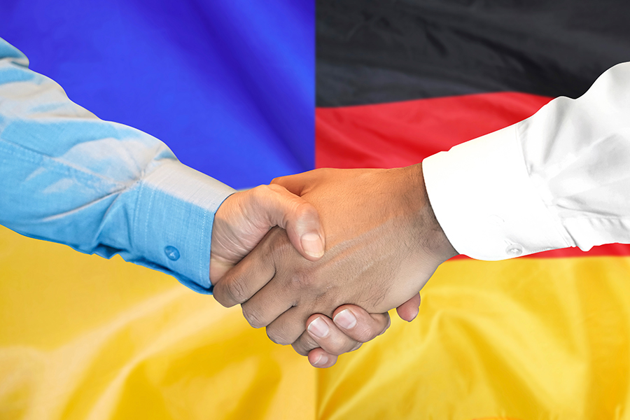 Händedruck auf deutschem und ukrainischem Flaggenhintergrund.