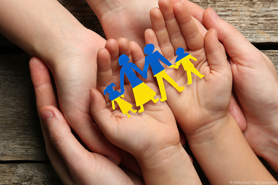 Drei übereinanderliegende Handpaare, in denen ein blau-gelber Scherenschnitt einer vierköpfige Familie liebt.
