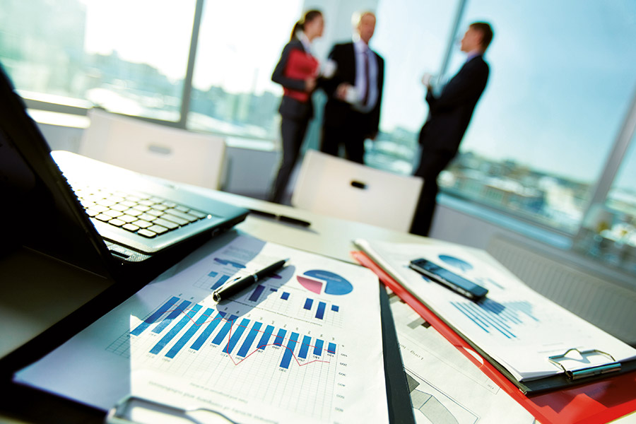 View of documents and calculations on a desk with three people in the background.