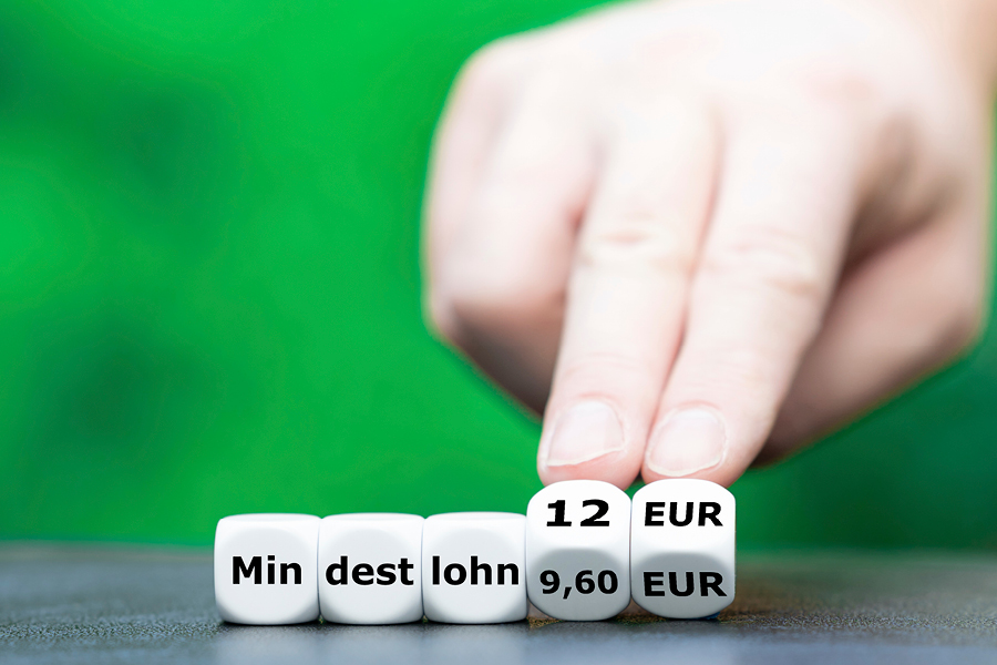 Würfel bilden das Wort Mindestlohn, eine Hand dreht die Würfel von 9,60 Euro auf 12 Euro.