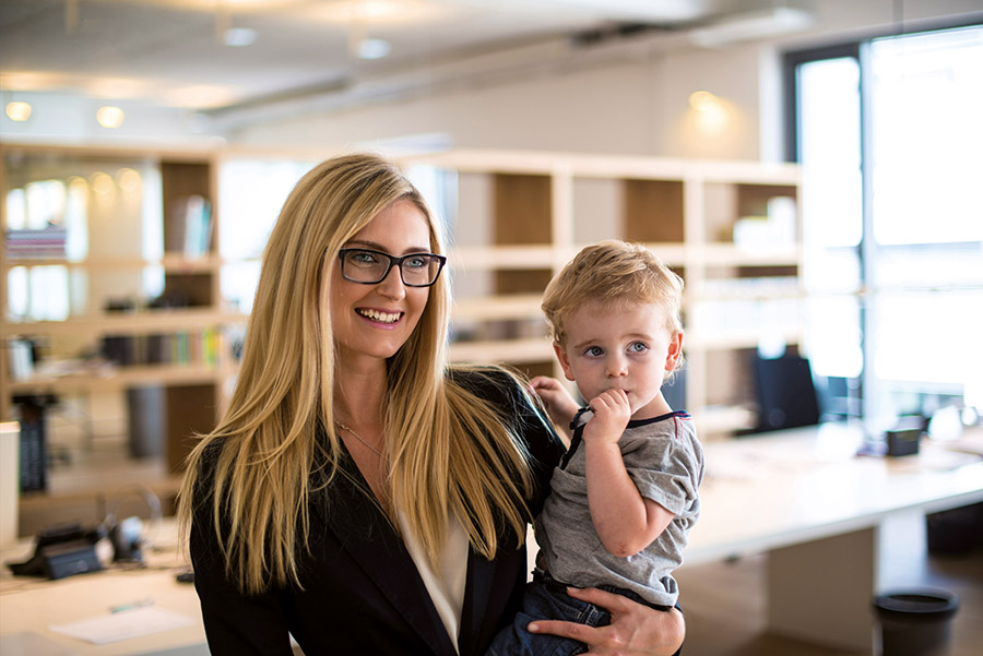 Geschäftsfrau steht mit ihrem Kind auf dem Arm in einem Büro