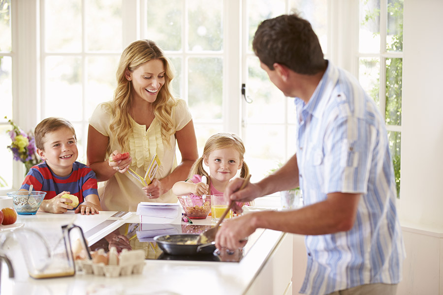 Eine vierköpfige Familie, Mutter, Vater, zwei Kinder, sitzen in der Küche und bereiten Frühstück zu