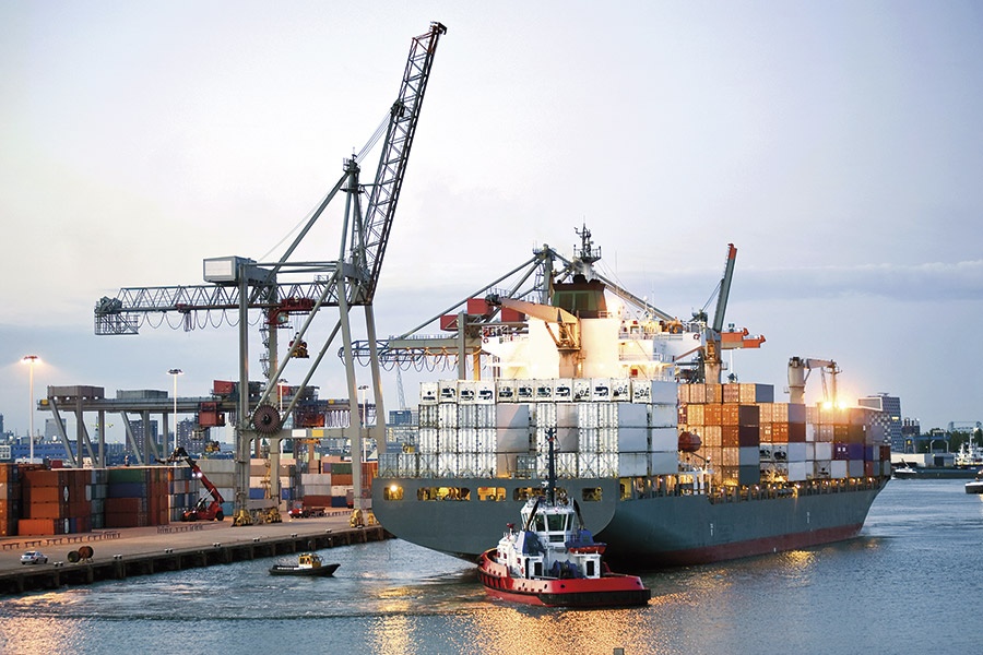 Small pilot boat guides large container ship into a port.