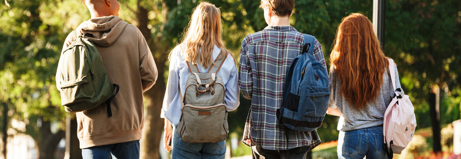 Das Foto zeigt vier Jugendliche von hinten, die auf einem Weg im Park laufen. Es sind zwei Jungen und zwei Mädchen in legerer Kleidung und mit Rücksäcken.