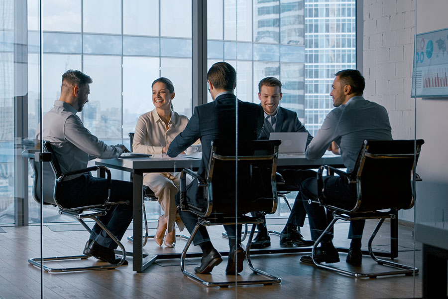 Vier Männer und eine Frau, alle in Businesskleidung, haben ein Meeting in einem hellen, modernen Besprechungsraum.
