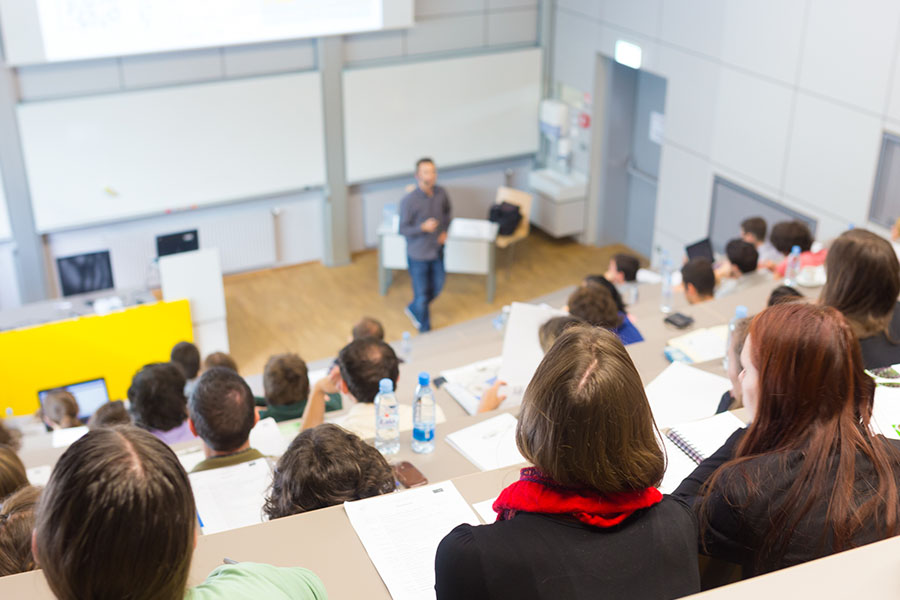 Blick von hinten oben in einen mit Studierenden gefüllten Hörsaal, in dem gerade eine Vorlesung stattfindet.