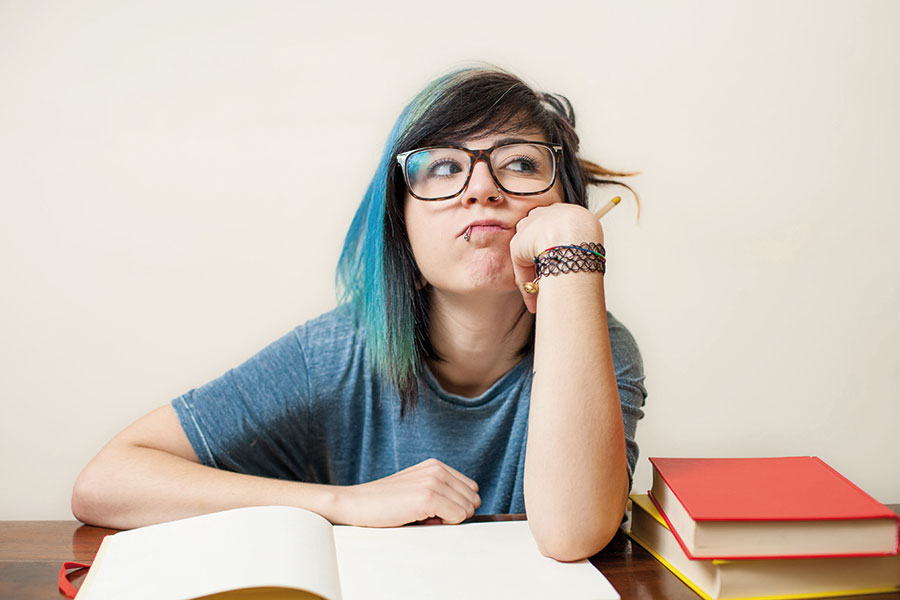 Young woman sits bored in front of her books and rolls her eyes.