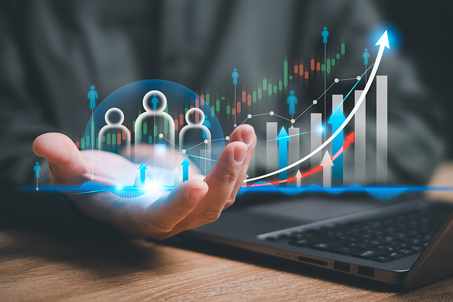 In einer virtuellen Darstellung schweben drei Personen-Icons sowie verschiedene Diagrammdarstellungen mit Aufwärts-Trend über der Hand eines Geschäftsmanns