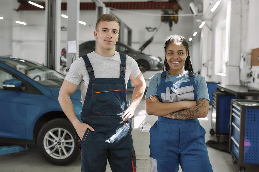 Zwei Auszubildende in einer Autowerkstatt schauen in die Kamera