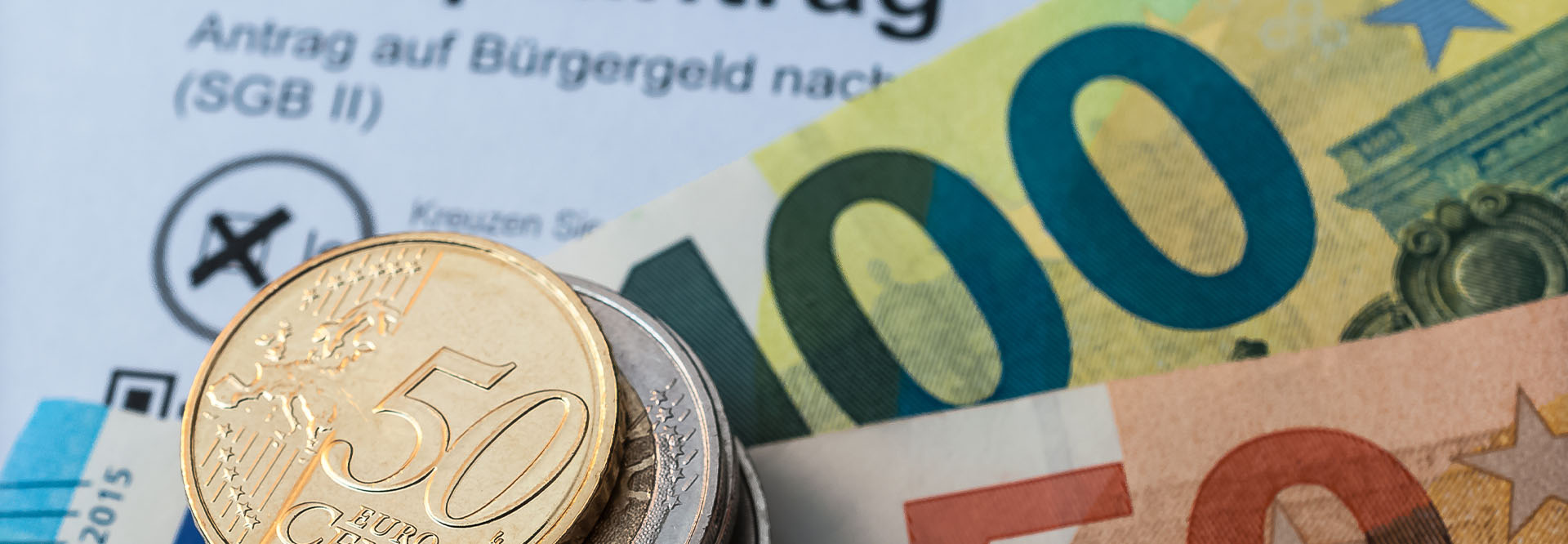 Ein Stapel Münzen und einige Euro-Scheine liegen auf einem Bürgergeld-Antrag.