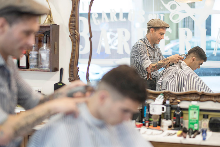 Tätowierter Friseur rasiert in einem Barbershop einem jungen Kunden den Nacken.