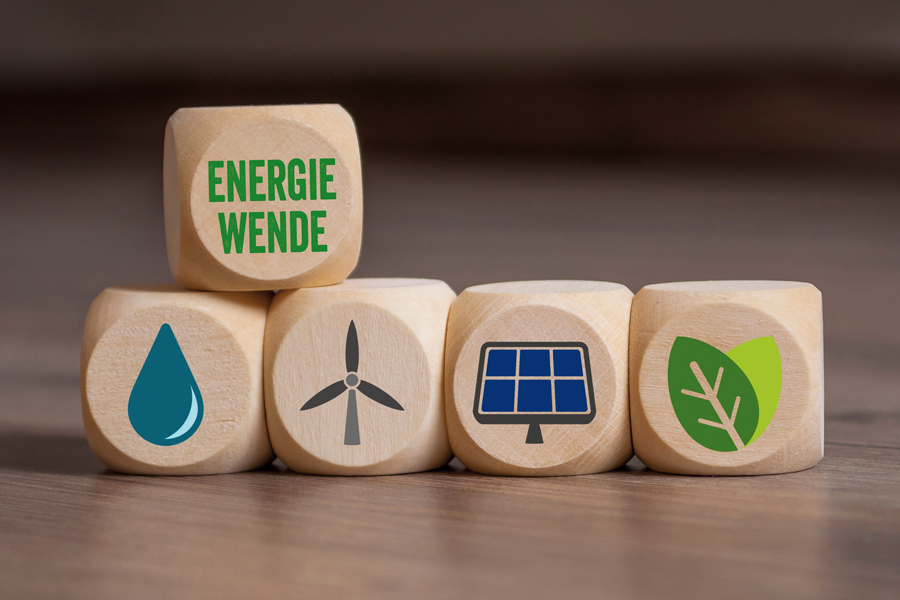 Vier Holzwürfel mit Symbolen für erneuerbare Energien liegen nebeneinander auf einem Holztisch. Auf dieser Reihe liegt ein einzelner Würfel auf dem das Wort „Energiewende“ geschrieben steht.