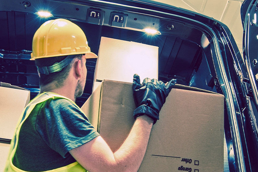 Man wearing a high-visibility vest and helmet is loading a box into a delivery truck.