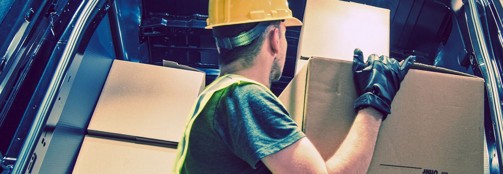 Man wearing a high-visibility vest and helmet is loading a box into a delivery truck.