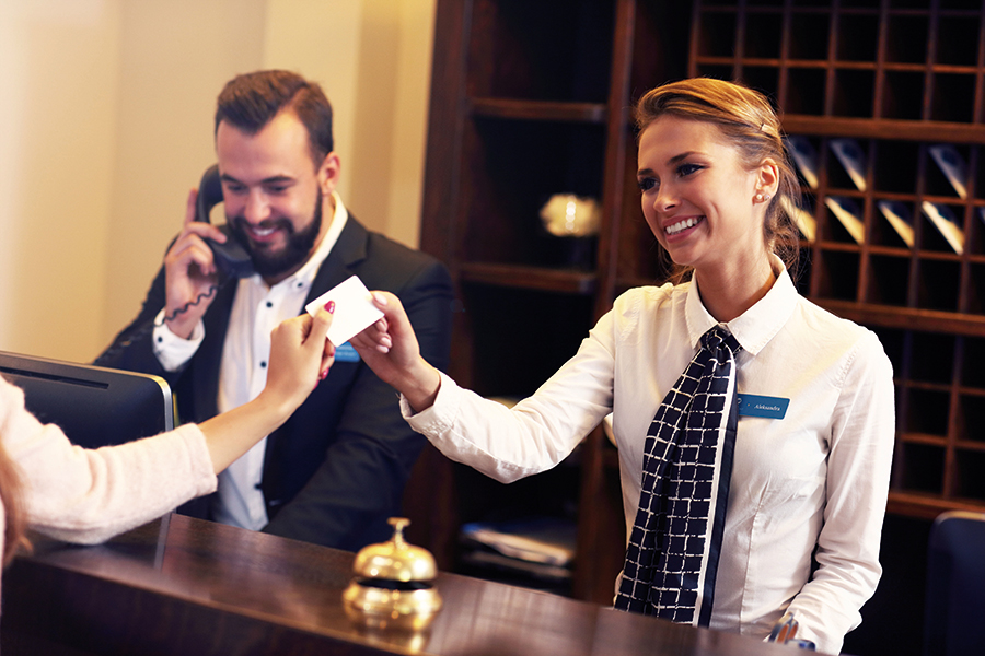 Angestellte eines Hotels übergibt dem Gast die Zimmerkarte. Der Kollege daneben telefoniert.