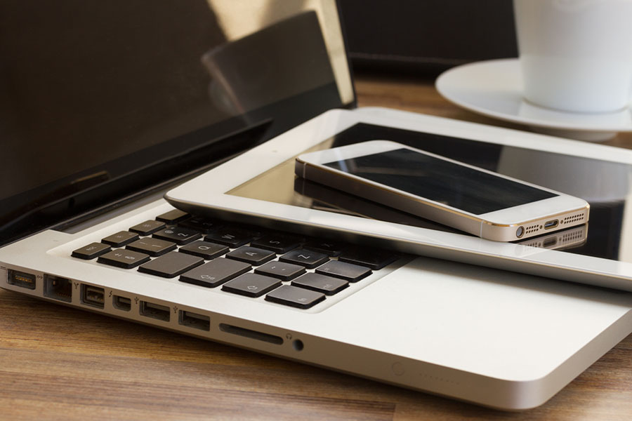 Auf einem Holztisch liegen gestapelt unten ein Laptop, darauf ein Tablet und oben ein Smartphone.
