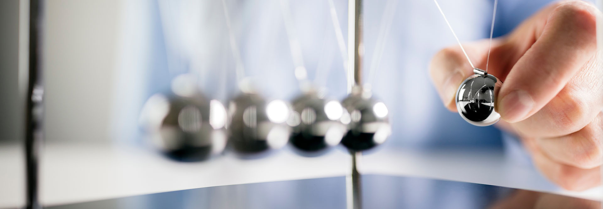 Männlich Hand, die die äußere Kugel eines Newtonpendels wegzieht um dieses anzustoßen.