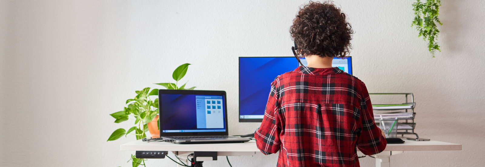 Shot from behind: young woman working standing at her height-adjustable desk, resting her left leg on an exercise ball.