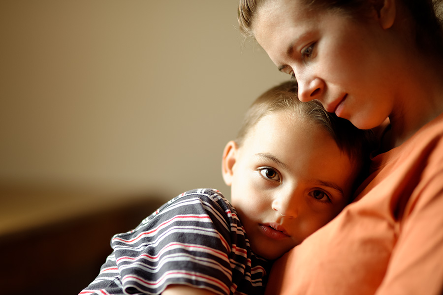 Ein Junge kuschelt sich auf den Brustkorb seiner Mutter und schaut traurig in die Kamera. Die Mutter lehnt ihren Kopf auf den seinen.