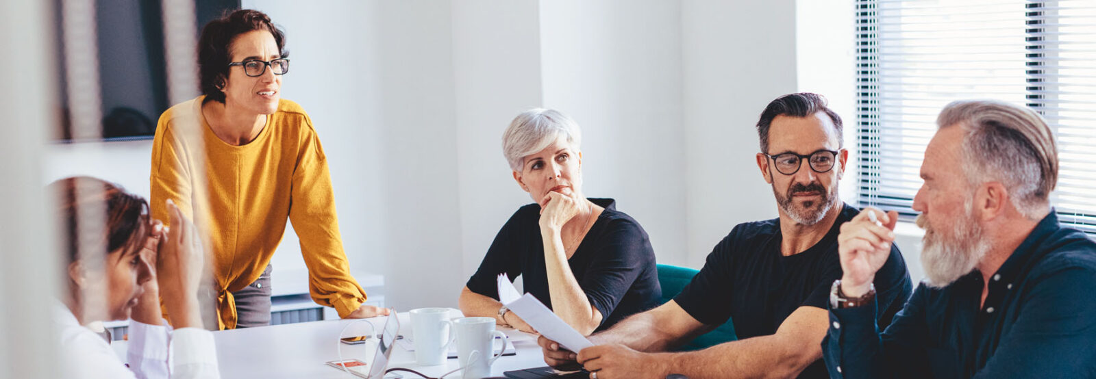 Three women and two men of mixed ages are sitting at a meeting table in an office.