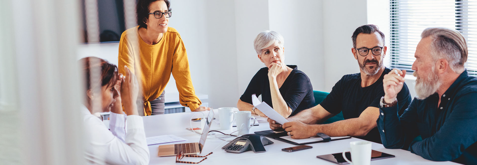 Drei Frauen und zwei Männer gemischten Alters sitzen in einem Büro an einem Besprechungstisch.