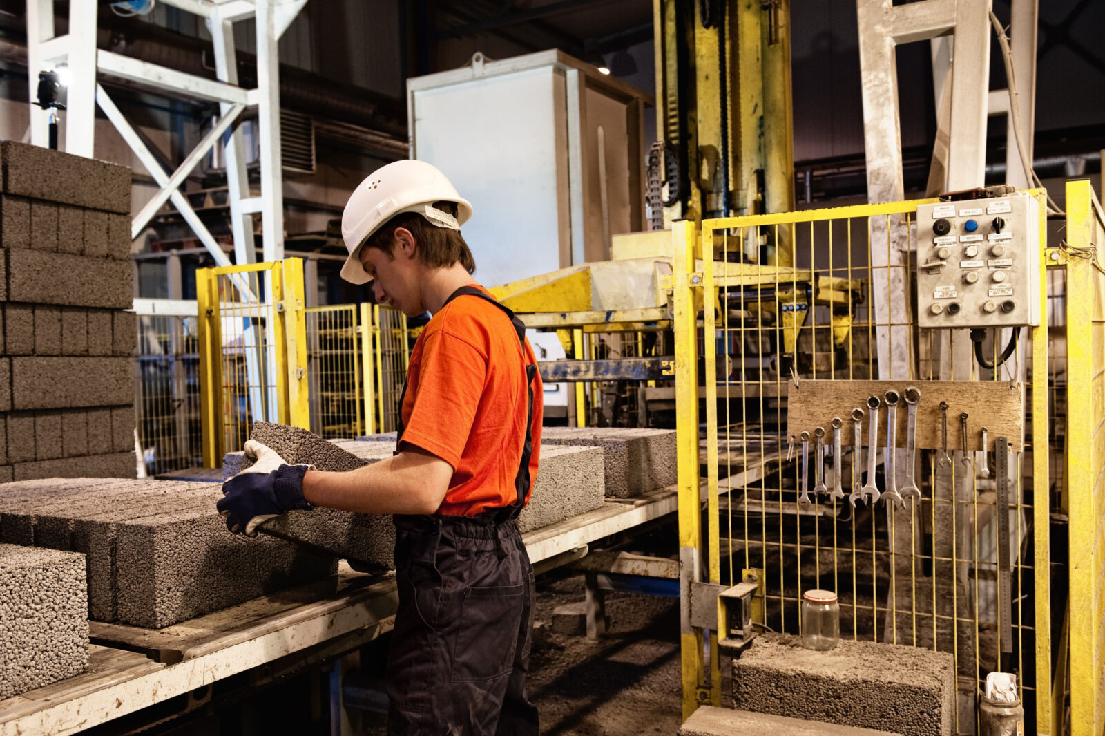 Alt-Text:Ein junger Mann in Arbeitskleidung steht in einer Werkshalle und stapelt Steine.