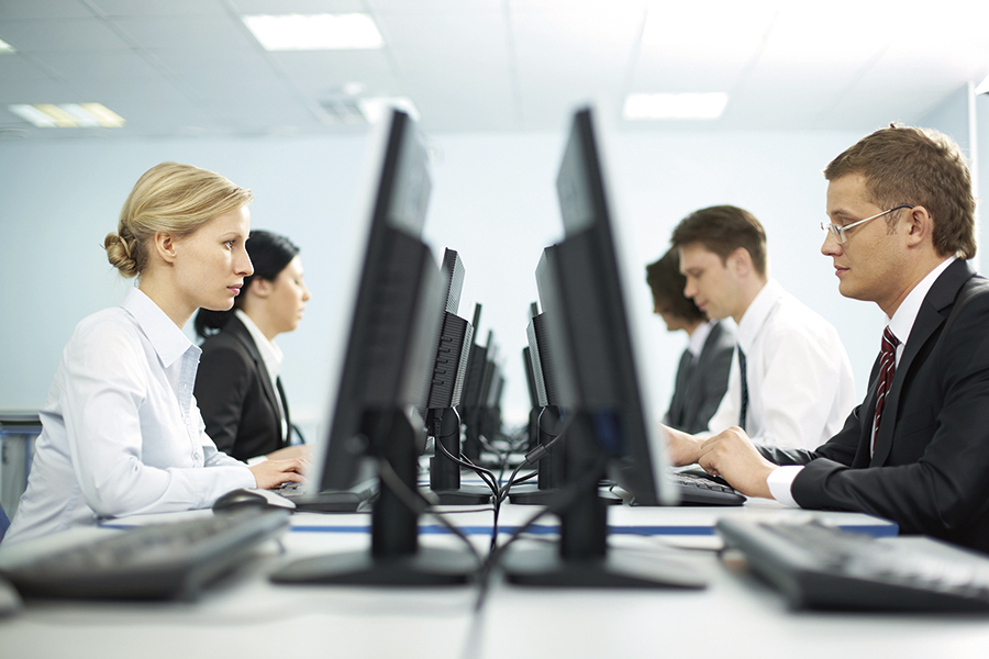 At a shared table, two women sit on the left side in front of their PC screens; two men sit on the right side in front of their PC screens.