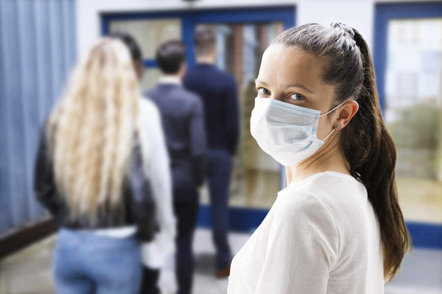 Woman wearing a face mask waits in line in front of a glass door.