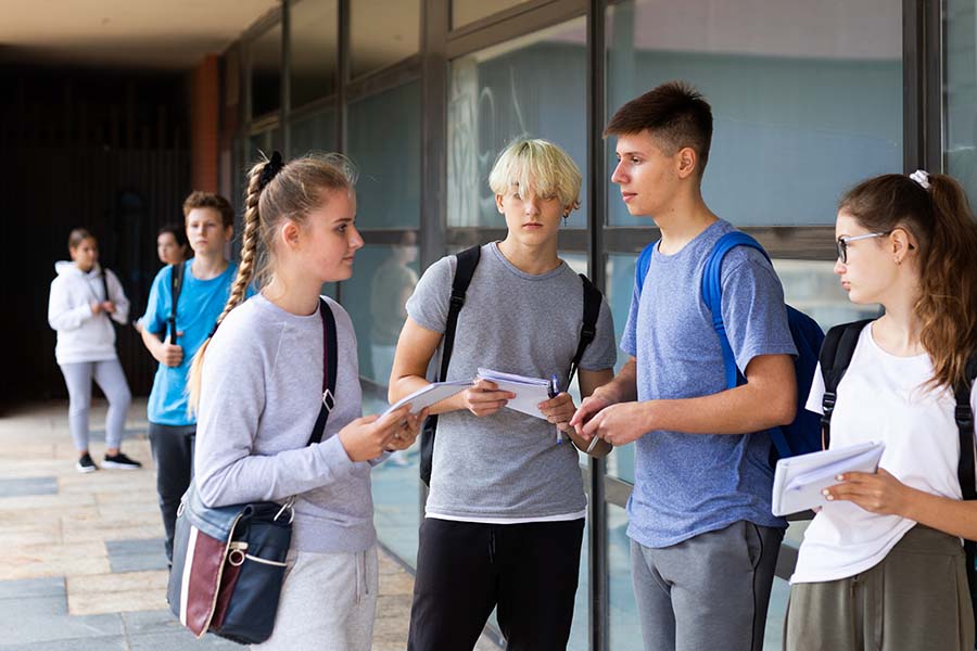 Eine Gruppe Jugendlicher, die vor dem Schulgebäude stehen und sich unterhalten.