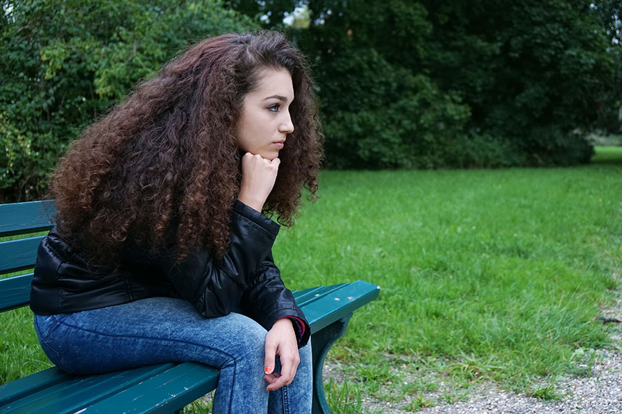 Ein ernst blickendes junges Mädchen sitzt im Park auf einer Bank.