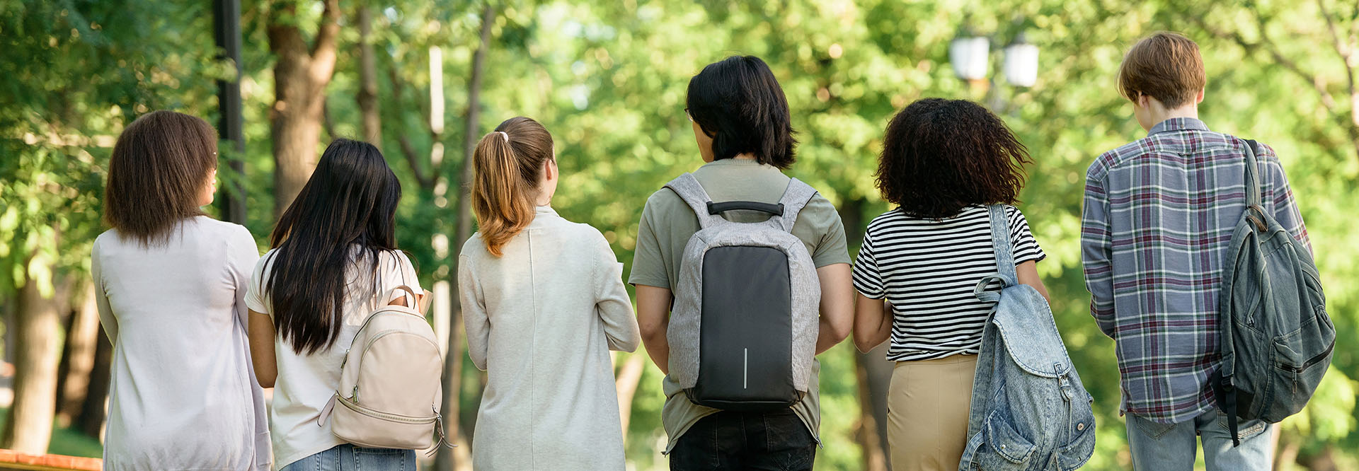 Rückansicht einer multiethnischen Gruppe von Jugendlichen, die durch einen sonnigen Park laufen.