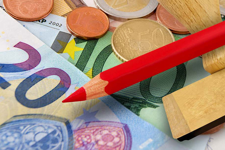 Ein roter Stift und ein Stempel liegen auf verschiedenen Euroscheinen und -münzen.