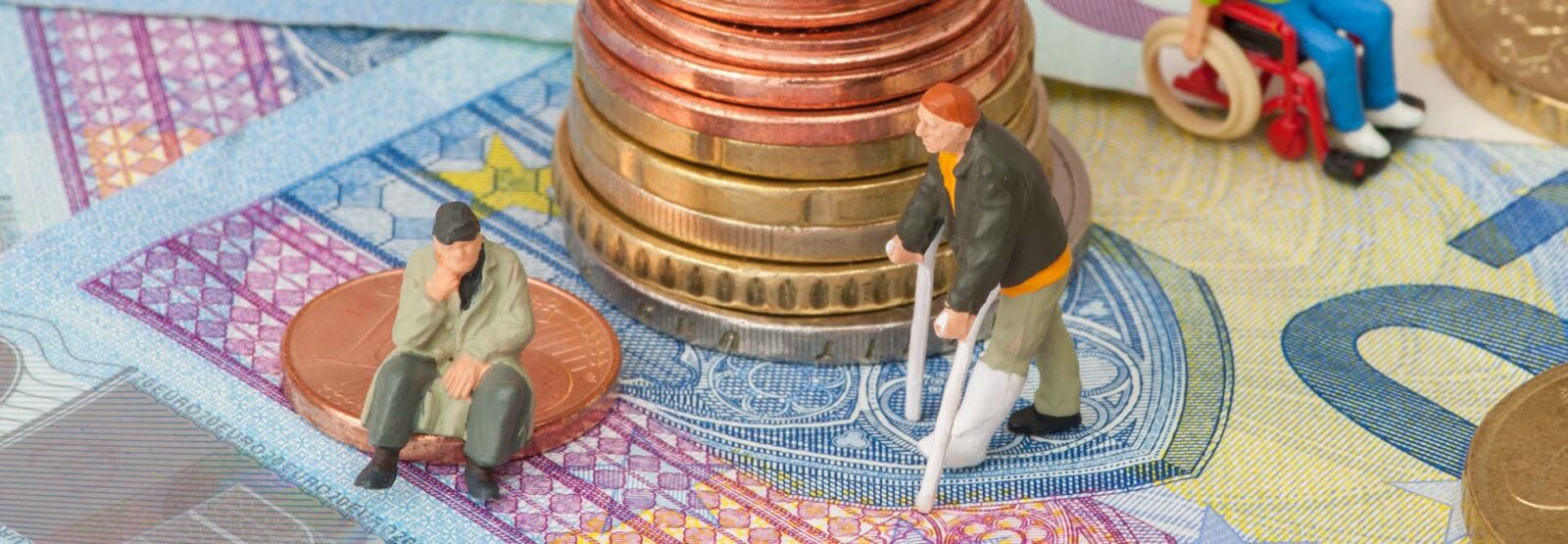 Miniaturfiguren von älteren Menschen oder solchen mit körperlichen Beeinträchtigungen auf einer Landschaft aus Geldscheinen und Münzen.