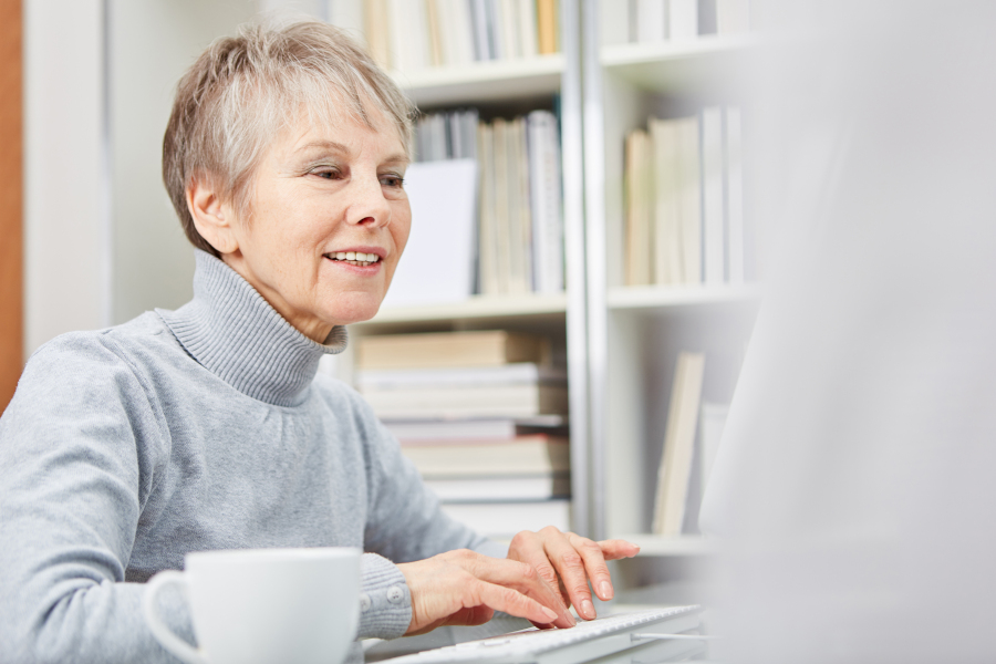 Seniorin arbeitet am Computer vor einem Bücherregal