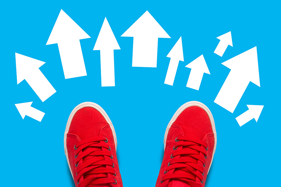 Blick von oben auf rote Turnschuhe, die auf einem hellblauen Hintergrund mit mehreren weißen Pfeilen stehen. Die Pfeile zeigen in verschiedenen Richtungen.