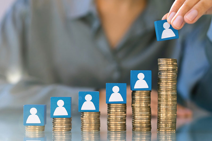 Hand greift Würfel mit Figur, der auf aufsteigenden Stapeln Geldmünzen steht.