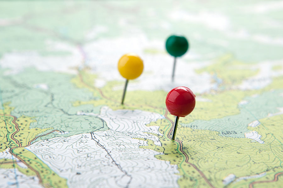 Topografische Karte mit bunten Reisbrettstiften als Ortsmarkierung.