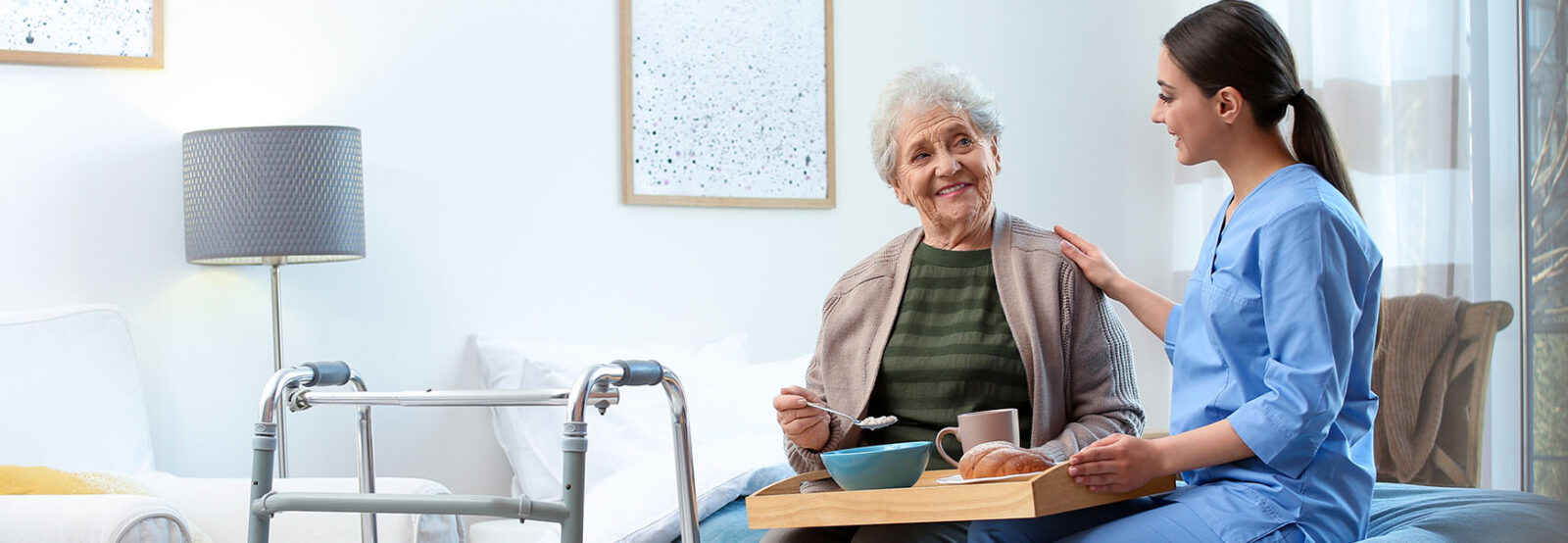 Junge Pflegerin betreut im Seniorenheim eine Seniorin beim Essen.