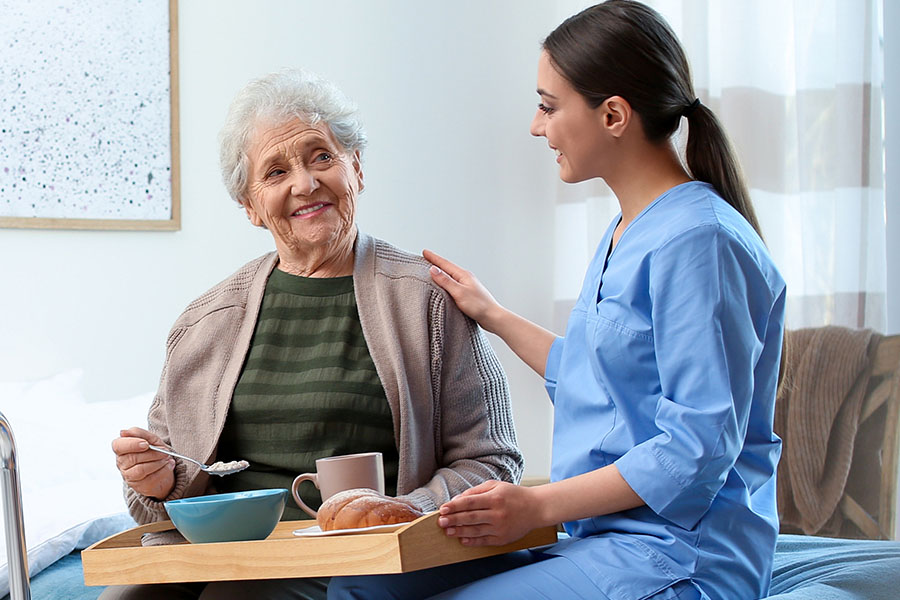 Junge Pflegerin betreut im Seniorenheim eine Seniorin beim Essen.