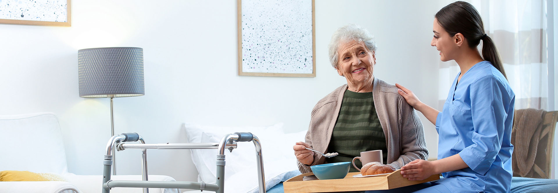 Junge Pflegerin betreut im Seniorenheim eine Seniorin beim Essen.