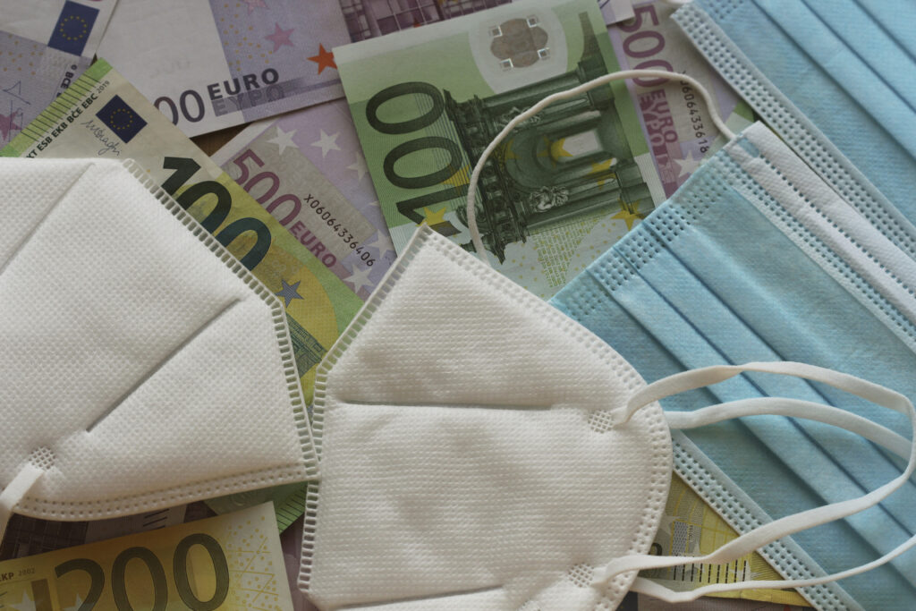 Verschiedene Mundschutzmasken liegen auf einem Tisch, auf dem 100€-, 200€- und 500€-Scheine ausgebreitet sind.