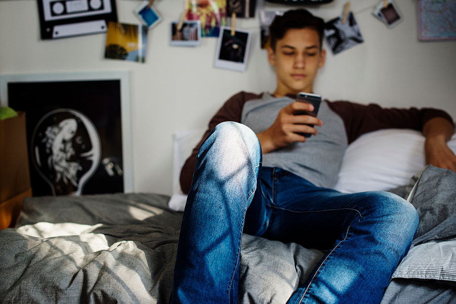 Jugendlicher sitzt mit seinem Smartphone auf seinem Bett.