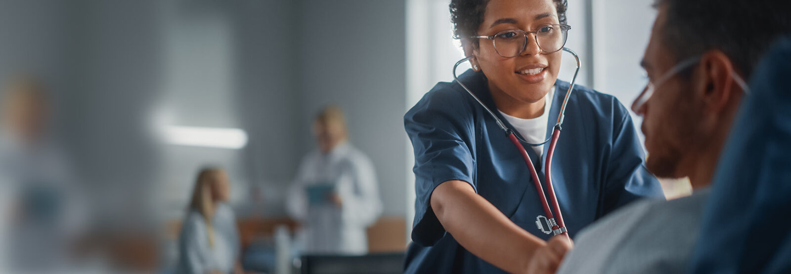 Krankenpflegerin untersucht mit Stethoskop das Herz eines Patienten.