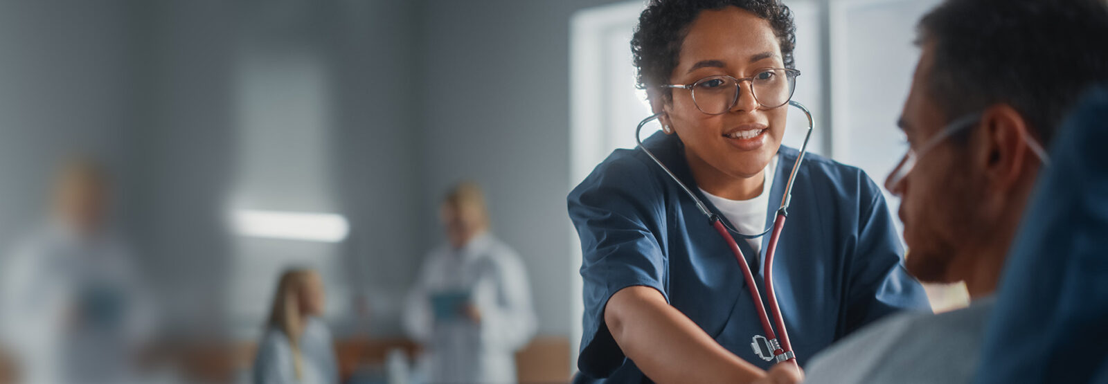 Krankenpflegerin untersucht mit Stethoskop das Herz eines Patienten.