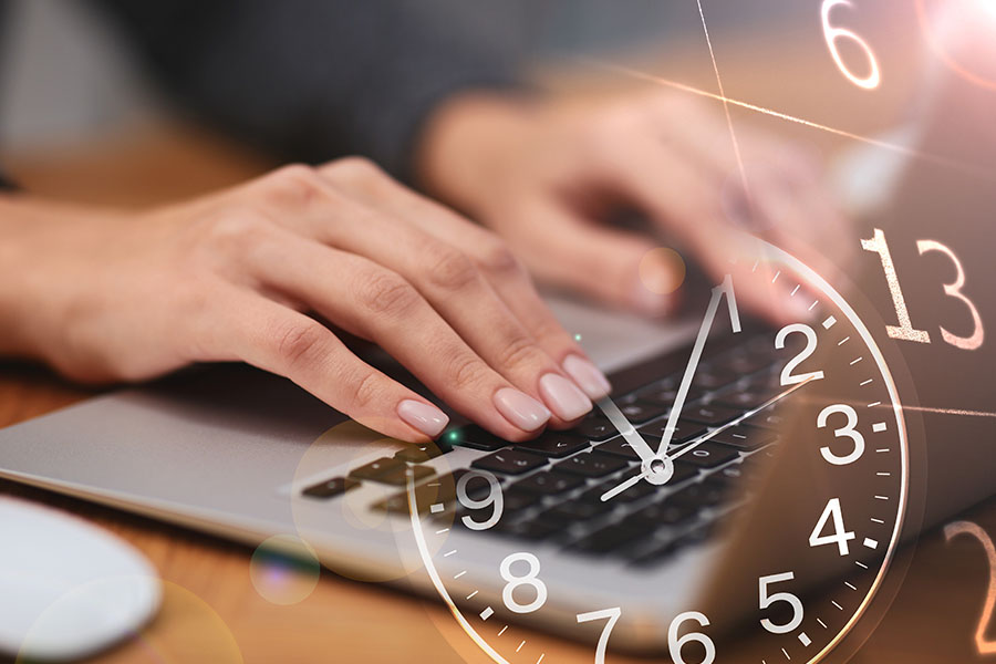 Die Nahaufnahme von weiblichen Händen, die auf der Tastatur eines Laptops tippen wird überblendet von dem Zifferblatt einer Uhr und einem Kalenderblatt.