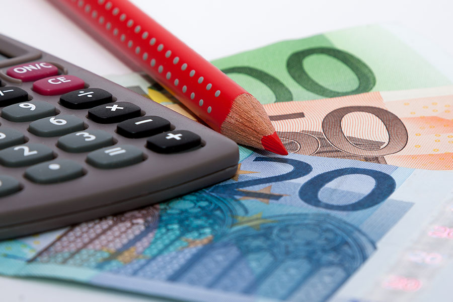 Roter Bundstift liegt auf mehreren Euro-Scheinen neben einem Taschenrechner.