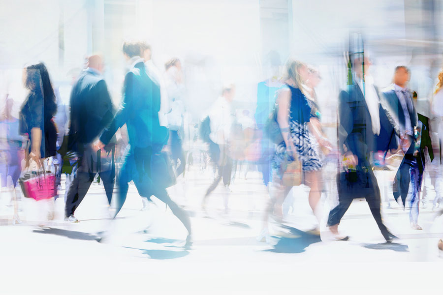 Numerous people, including many businesspeople, cross a street in a big city on a sunny day. Panoramic shot with motion blur.