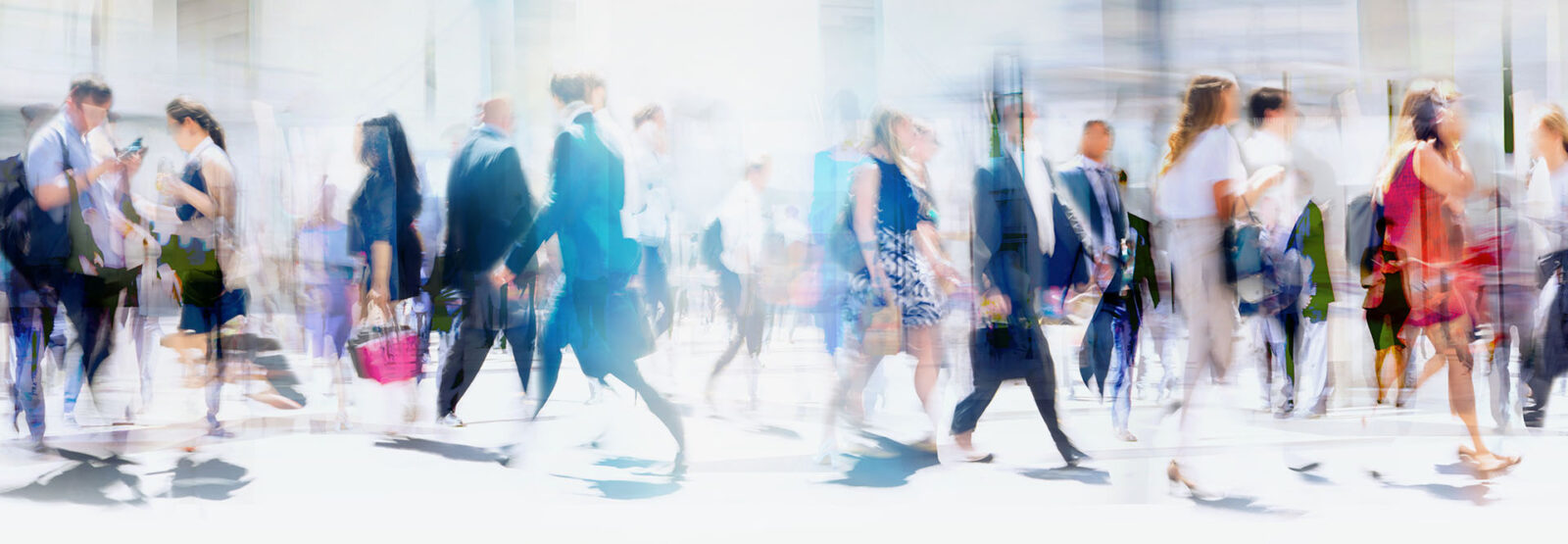 Numerous people, including many businesspeople, cross a street in a big city on a sunny day. Panoramic shot with motion blur.
