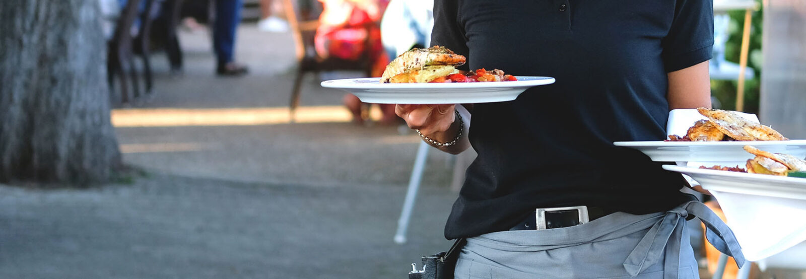 Eine Kellnerin trägt Teller mit Speisen durch den Außenbereich eines Restaurants.